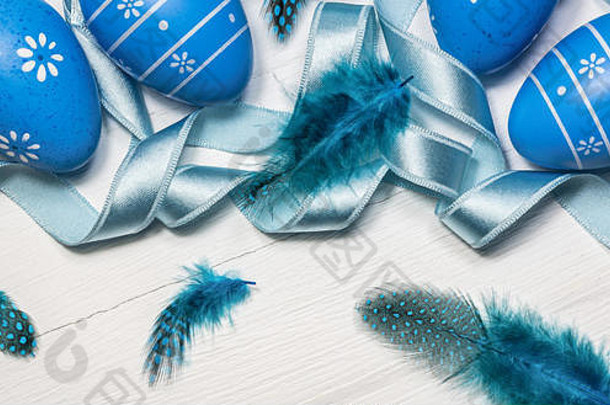 复活节背景，白色木桌上有蓝色的鸡蛋、羽毛和缎带。特写镜头，横幅照片。
