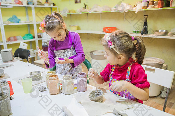 在陶瓷工作室的桌子上，两个年轻的艺术家女孩用画笔画着粘土花瓶