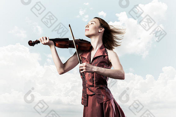 身着红色服装的女小提琴手在多云的天空中演奏旋律