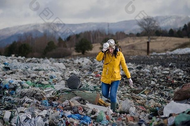 戴着防毒面具在垃圾填埋场上行走的妇女，环保理念。