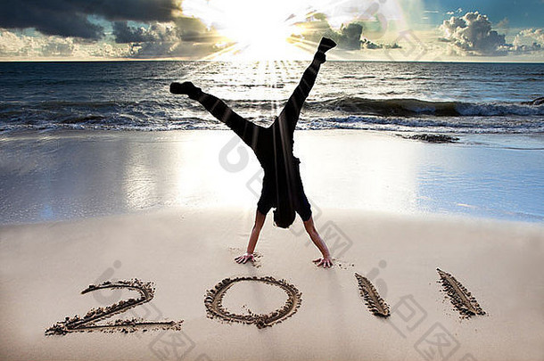 2011年新年快乐，在日出的海滩上。年轻人倒立并庆祝。