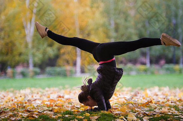 在秋季公园里，一个正在表演体操的女孩双手站立