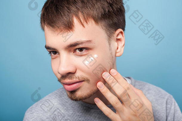 年轻黑发男子的肖像，留着小胡子和小胡子，在眼睛下涂抹面霜，治疗或润肤化妆品，护肤概念。我