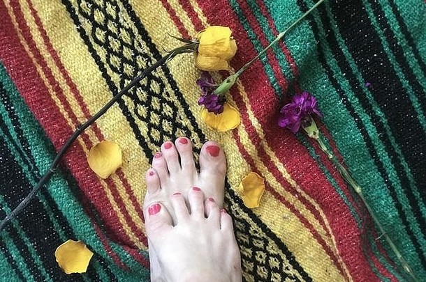一个女人的脚放在一条有花瓣的喜庆多彩的毯子上。脚和花
