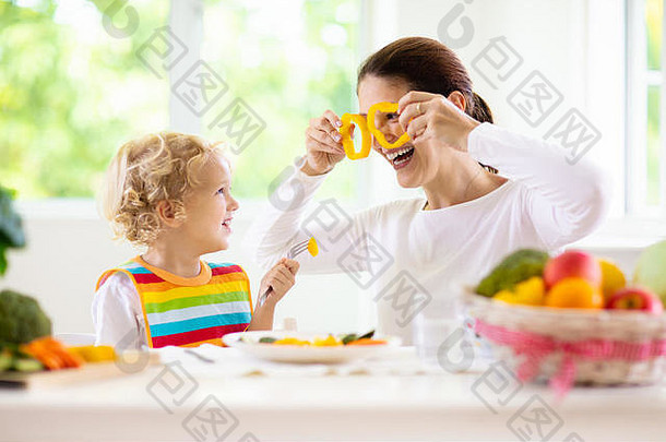母亲给孩子喂蔬菜。<strong>妈妈</strong>在有窗户的白色<strong>厨房</strong>里喂孩子。坐在高脚椅上的，吃着健康的蒸胡萝卜和土豆午餐