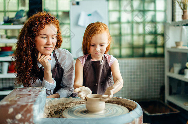 红头发的母亲和她的小女儿在陶轮上用粘土浇铸