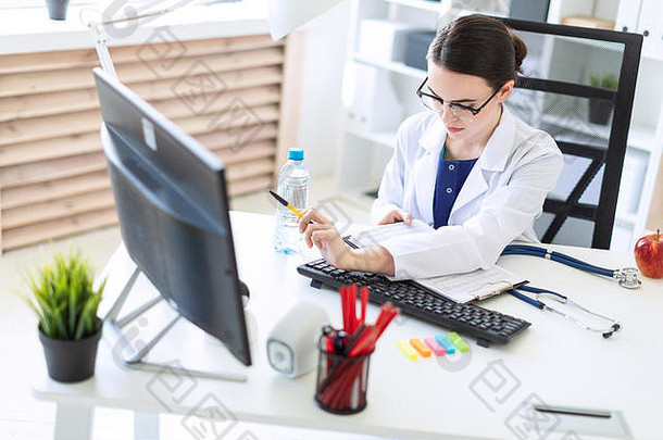 一个穿着白色长袍的漂亮女孩坐在电脑桌旁，手里拿着<strong>文件</strong>和钢笔。