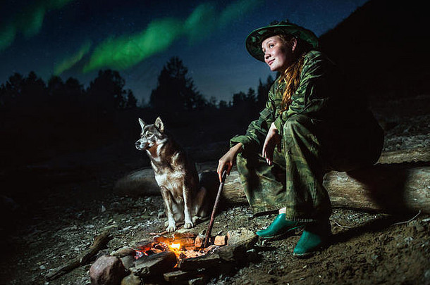 在星光和北极光下，童子军和她的狗围着篝火