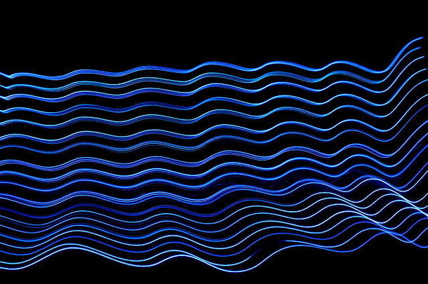 在黑色背景下以抽象波浪图案拍摄的霓虹蓝色长曝光照片。光绘摄影，抽象色彩