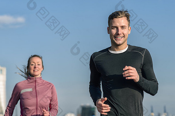 一位面带微笑的帅哥和他的妻子在健康和健身理念中慢跑，在晴朗的蓝天下俯瞰上身的低角度视图