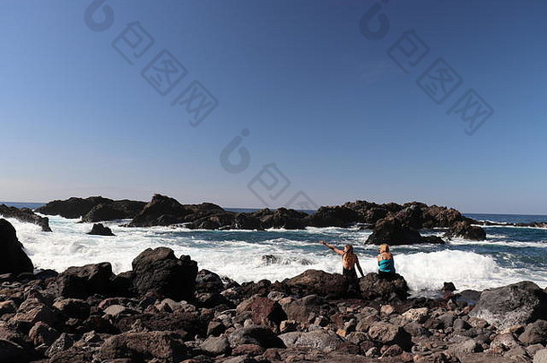 加那利群岛特内里费岛海滩上，两个人在岩石上聊天