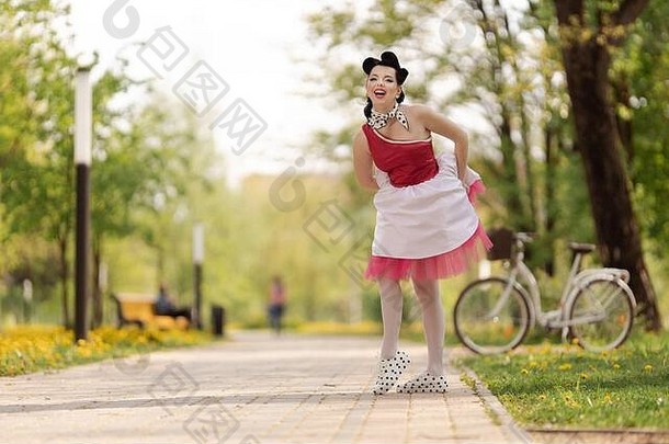 阳光明媚的日子里，一个穿着粉色连衣裙、留着40-50年代发型的美丽女孩在公园里跳舞、摆姿势。复古风格的照片。