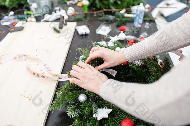 妇女系着蝴蝶结丝带，装饰着圣诞花环。用胶固定玩具和装饰。双手特写。制作装饰饰品的硕士班。