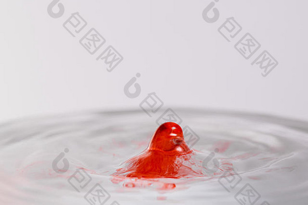 一个红色的水的特写镜头，类似于血，水滴溅入浅色的白灰色背景中