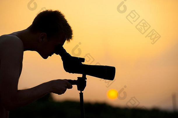 黄昏时，一个肌肉发达的男孩通过望远镜观看