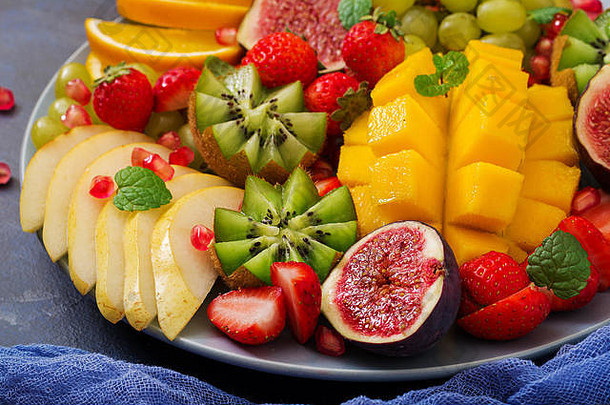 把水果和浆果放在盘子里。芒果、猕猴桃、无花果、草莓、葡萄、梨和橙子。纯素菜肴。饮食菜单。