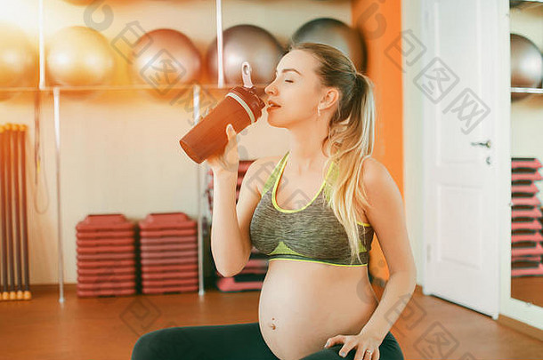 孕妇瑜伽。年轻漂亮的怀孕女孩坐在健身球上喝瓶子里的水