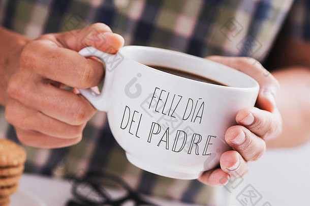一个白人男子的特写镜头，手里拿着一个白色的陶瓷杯，杯里放着咖啡，上面用西班牙语写着“父亲节快乐”，