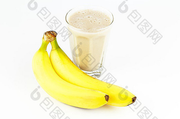 两个长长的黄色甜水果放在一杯水果旁边。在香蕉泥液体旁边的白色表面上放着两个完整的未去皮的黄色香蕉