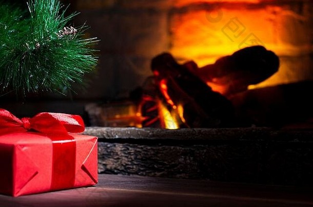 圣诞树下的一个红色礼品盒，放在一个靠近火场的木桌上
