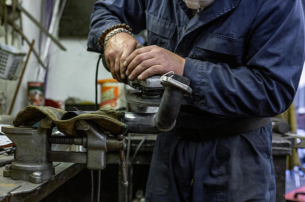 重型工业工人在汽车维修厂用角磨机切割钢材。