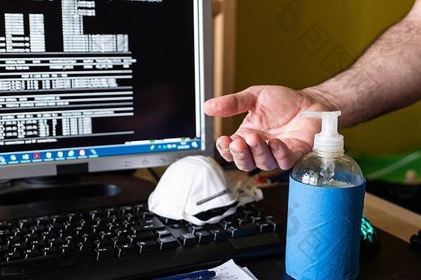 冠状病毒大流行时在家工作。将口罩放在键盘上，分发消毒凝胶，对双手进行消毒。