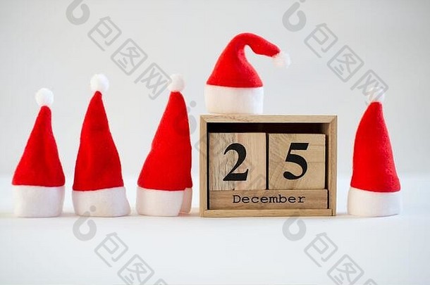 立方体木制日历，显示12月25日的日期，白色背景上有小圣诞老人帽。降临节日历、圣诞节背景、空间