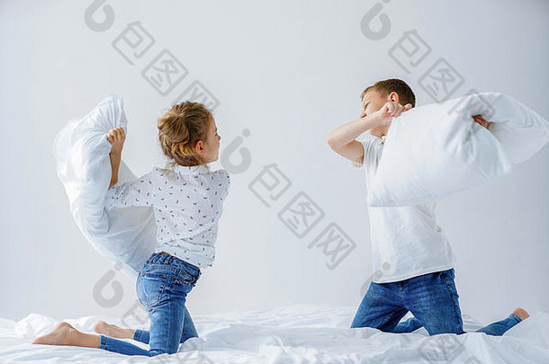 淘气的双胞胎女孩男孩友好的战斗上演了枕头战斗床上卧室种类游戏