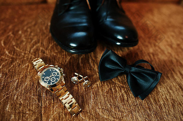 新郎的婚礼黑色鞋子，金色手表，领结和袖扣放在地上。