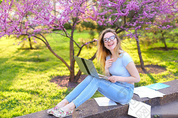 快乐的女学生在花开的公园里用笔记本电脑和<strong>试卷</strong>准备考试。