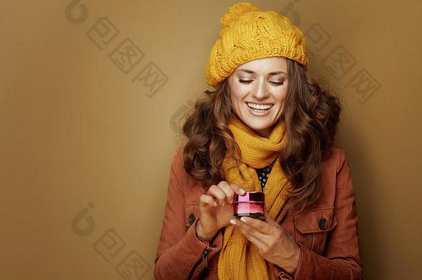 你好，秋天。40岁的女子在贝雷帽和围巾打开瓶的面霜在青铜背景。