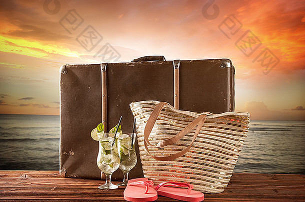 携带旧行李箱和配件的夏季旅行理念。背景上的模糊海滩