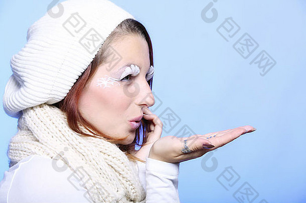 有创意的冬装吹吻的年轻女子肖像。暖和的衣服。冬季和圣诞节的概念。蓝色背景