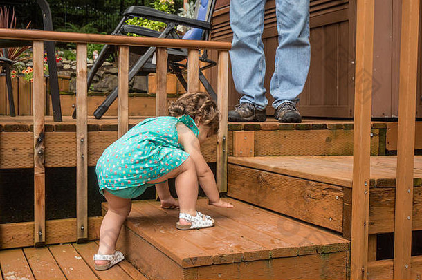 一个14个月大<strong>的</strong>蹒跚学步<strong>的</strong>小女孩在后院<strong>的</strong>雪松甲板上艰难地爬上木台阶，她<strong>的</strong>祖父在一旁看着