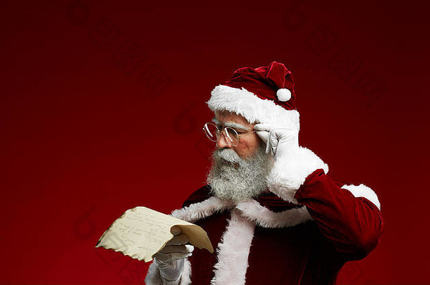 经典圣诞老人的肖像，羊皮纸上的阅读清单和调整眼镜，同时站在红色背景下，空间