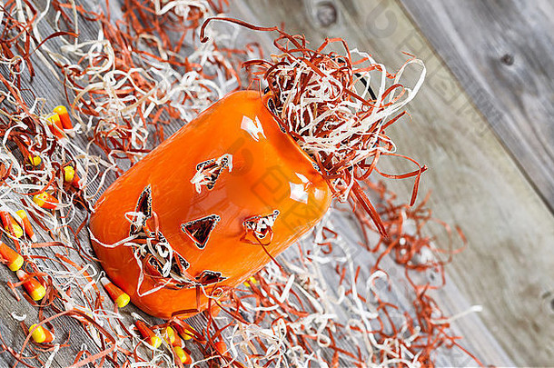 特写角度的水平图像，一个可怕的橙色南瓜罐，装满碎纸，放在粗糙的木板上