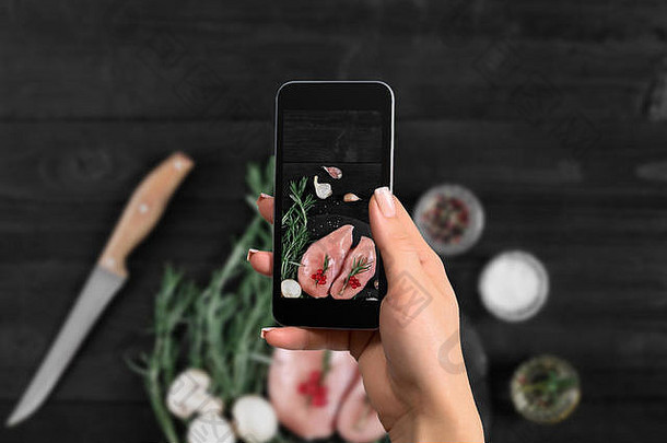 女手智能手机使照片生鸡乳房黑色的背景新鲜的蘑菇大蒜草本植物
