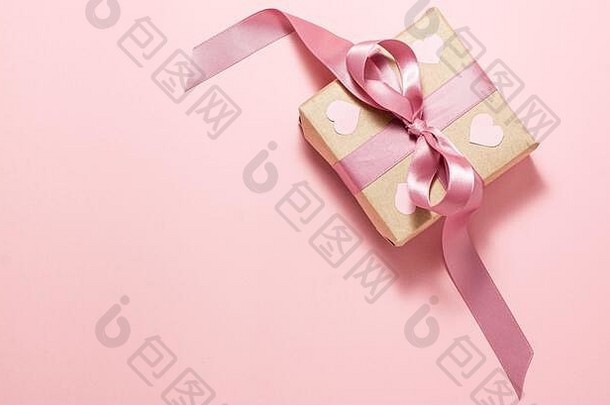 棕色纸礼品盒，带紫色丝带蝴蝶结，右侧粉红色背景上有四个粉红色心形。情人节的概念。平铺顶六