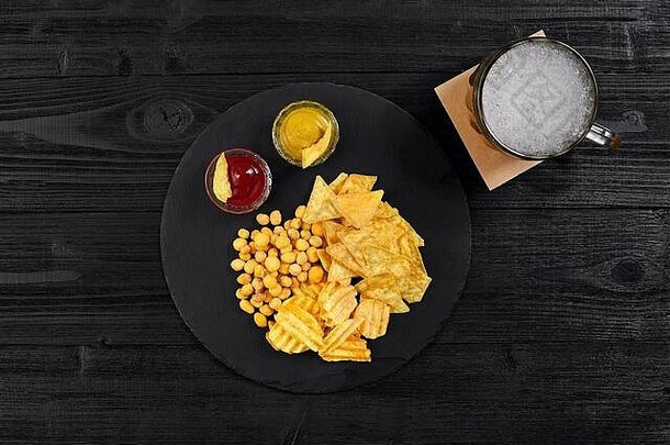 黑木桌上啤酒杯和带酱汁小吃的俯视图。