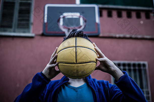 一个少年在一座老房子的院子里用篮球捂住脸