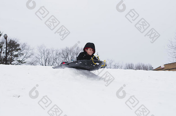 一个男孩坐着雪橇从白雪覆盖的小山上滑下来。