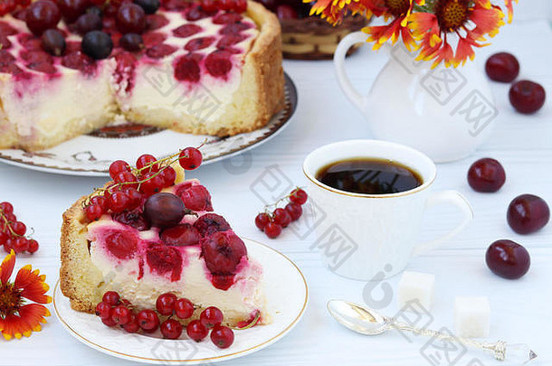 带浆果的蛋糕放在白色背景的盘子上，前景是一块蛋糕和一杯咖啡