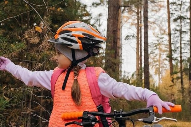 一个白人孩子在秋天公园里骑自行车散步。小女孩在森林里骑着<strong>黑橙</strong>色的自行车。这孩子去做自行车运动。骑自行车的运动骑乘