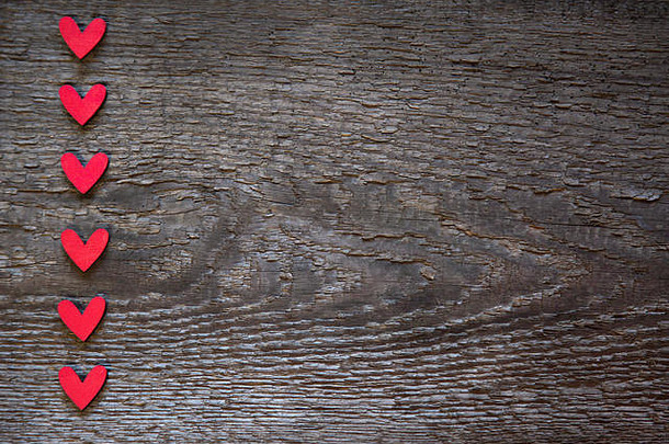 红色的心垂直地排列在一块古老的棕色干木板的左边。情人节贺卡