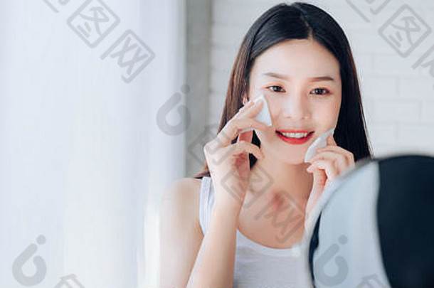 年轻的美亚洲女人清洁脸棉花镜子护肤品微笑白色卧室复制空间