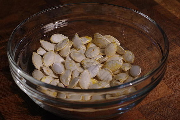橡木砧板上一个玻璃碗的干<strong>南瓜</strong>籽的微距照片。健康饮食小吃。阿伯丁，苏格兰，英国。