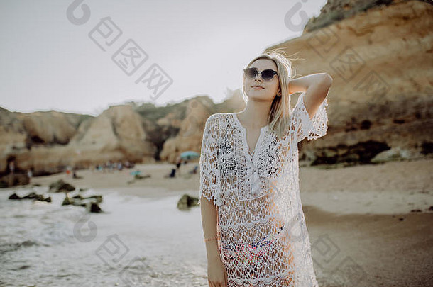 穿着休闲夏装的时髦女人在水线边散步，在沙滩日落或海洋日出时看着海浪。