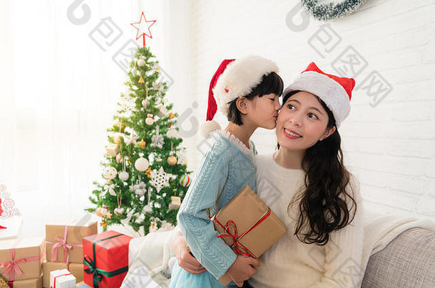 快乐的亚洲小女孩给了妈妈一个吻，感谢她送给妈妈家里的圣诞礼物。