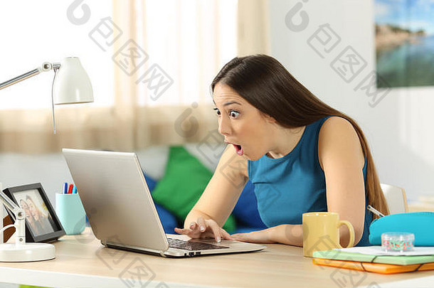 一个单身学生坐在她房间里的桌子上，用笔记本电脑在网上搜索内容