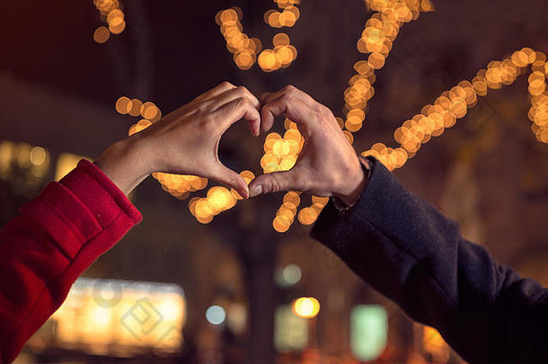 情侣们在圣诞灯饰上用手塑造心形